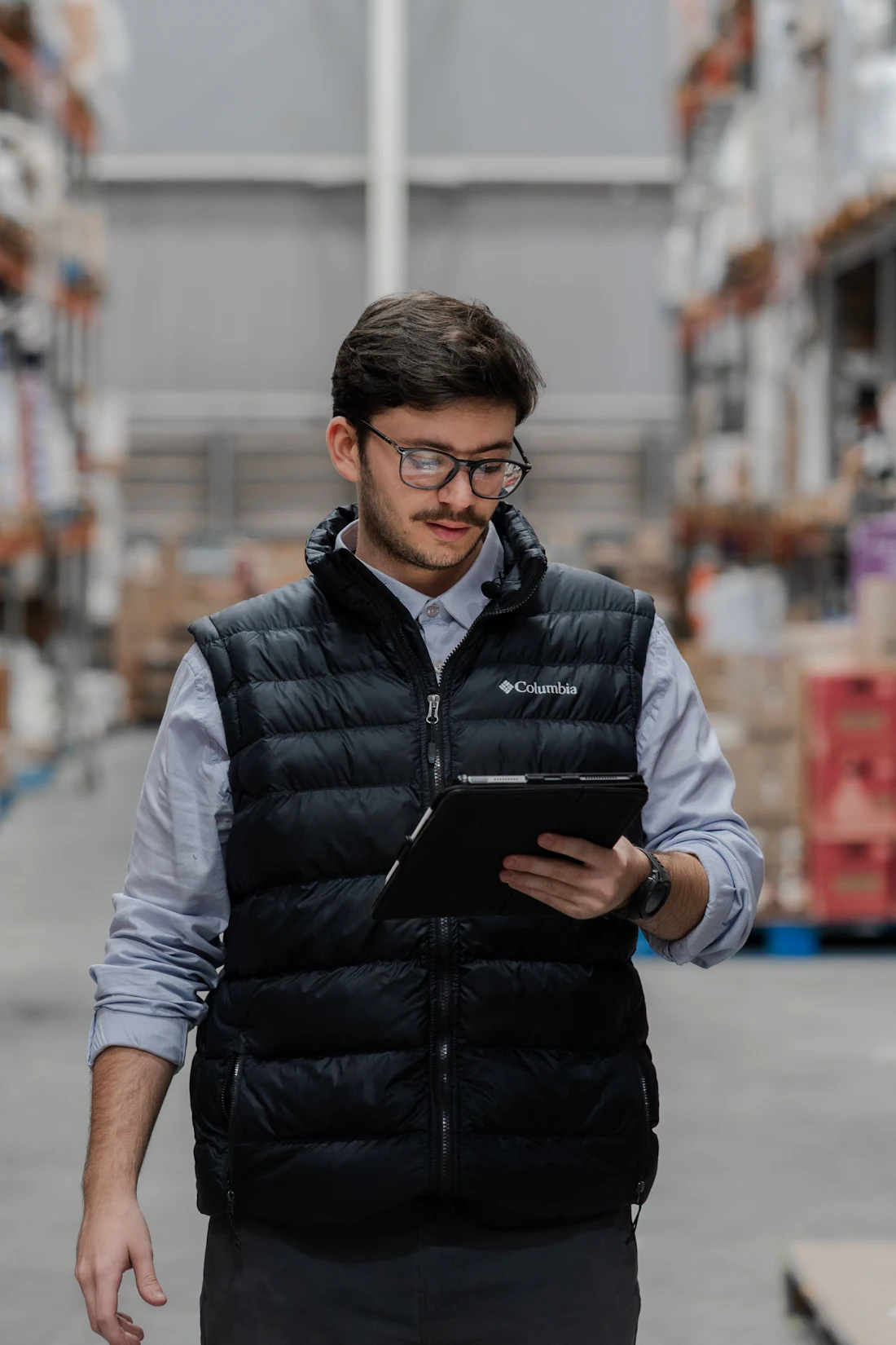 A warehouse operator reading a tablet while walking a pick aisle